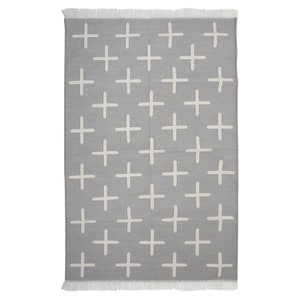 May include: A rectangular gray rug with a repeating pattern of white plus signs. The rug has a fringe on the top and bottom edges. The design is simple and modern, suitable for various interior styles.