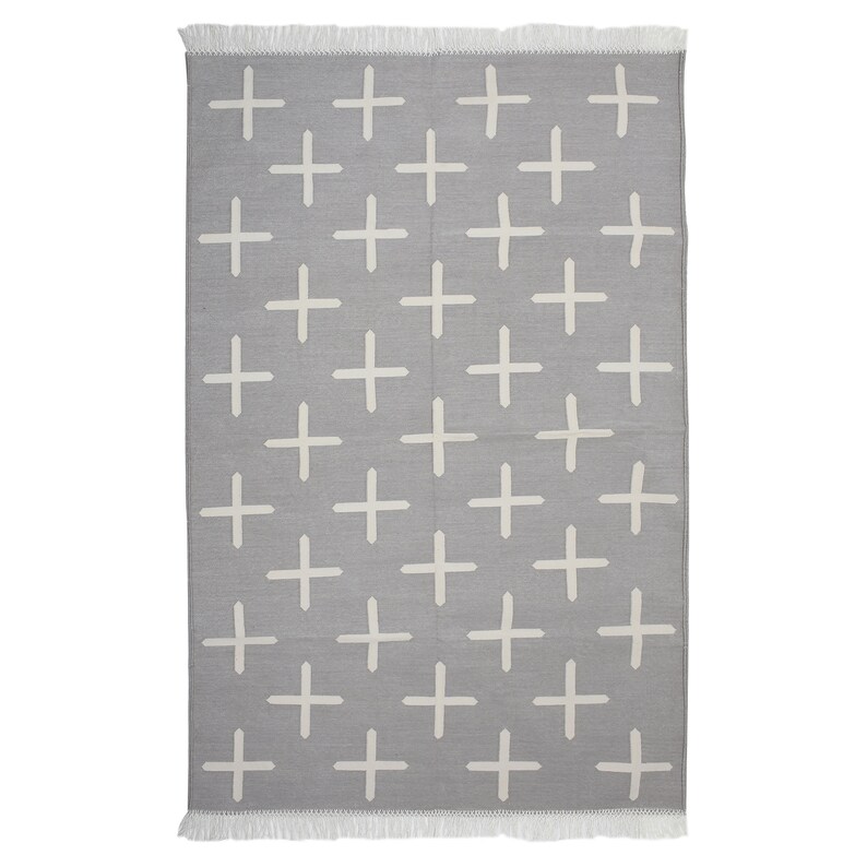 May include: A rectangular gray rug with a repeating pattern of white plus signs. The rug has a fringe on the top and bottom edges. The design is simple and modern, suitable for various interior styles.