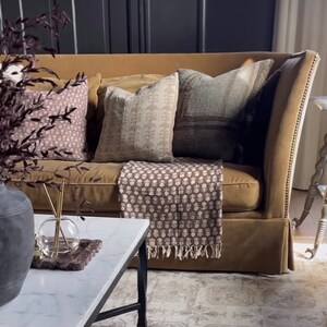 Puede incluir: Un sof&aacute; de terciopelo marr&oacute;n con una manta de tiro con estampado marr&oacute;n y blanco y tres almohadas. Las almohadas son de color marr&oacute;n claro con un patr&oacute;n blanco, marr&oacute;n oscuro con un patr&oacute;n blanco y azul claro con un patr&oacute;n marr&oacute;n.