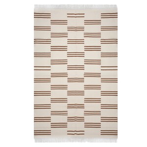 May include: Rectangular cream-colored rug with a repeating pattern of three horizontal brown stripes. The rug has a fringed edge at the top. The design is a grid of alternating cream and brown rectangular blocks.