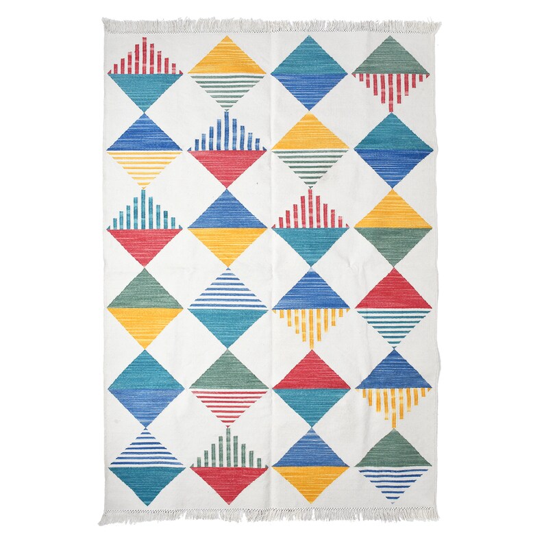 May include: White rectangular rug with a repeating diamond pattern in red, yellow, blue, and green. Each diamond contains either horizontal or vertical lines. The rug has a fringed edge.