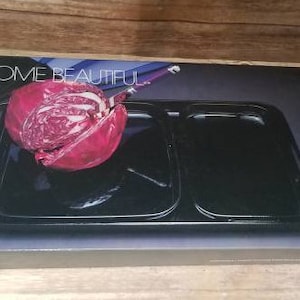 Puede incluir: Un molde para hornear negro con dos compartimentos, uno más grande que el otro. El molde está sobre una caja con las palabras "Home Beautiful" impresas en ella. Una col roja está en el compartimento más grande.