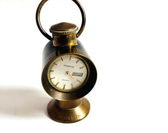 May include: A vintage brass-toned quartz clock with a circular face, featuring the text "renecta" and "MON". The clock has a handle and a base with the text "TURRIS". The clock is a unique decorative item.