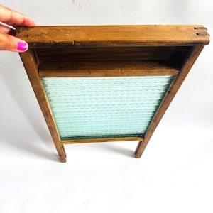Puede incluir: Un antiguo lavadero de madera con una superficie de lavado estampada en azul claro y blanco. El lavadero está hecho de madera y tiene un marco rectangular con un diseño inclinado. El lavadero es una herramienta de lavandería clásica.