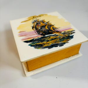 Peut inclure: Une boîte en bois avec un couvercle blanc représentant un navire naviguant sur l'océan au coucher du soleil. Le mot "Love" est écrit au-dessus du navire.