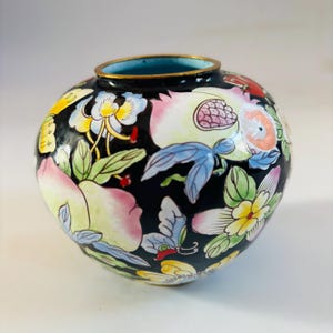 May include: A round, black ceramic vase with a gold rim and a blue interior. The vase is adorned with colorful floral and butterfly designs in pink, yellow, blue, and green.