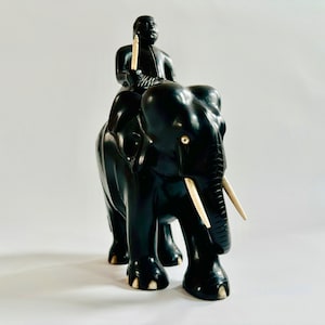 May include: A black wooden sculpture of an elephant with ivory tusks. A small black figure is riding on the elephant's back.