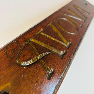May include: A wooden sign with the word "AVON" carved into it. The letters are painted gold and stand out against the dark brown wood. The sign has a rustic, vintage appearance.
