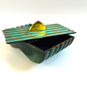 May include: A green and gold metal box with a ribbed design and a triangular lid. The box is open and the lid is propped up.