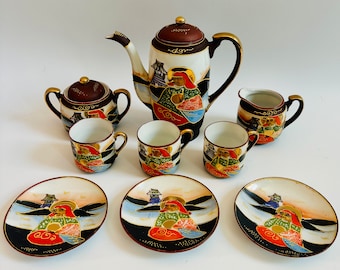 May include: A set of Japanese teacups and teapot with intricate floral and figure designs. The teapot is brown with gold accents and the cups are white with gold and red accents.