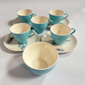 Könnte beinhalten: Ein Set aus sechs Vintage-Teetassen und Untertassen. Die Tassen sind leuchtend türkis mit cremefarbenen Innenräumen. Die Untertassen sind cremefarben mit einem türkis-schwarzen Baumdesign. Eine türkisfarbene Schüssel ist ebenfalls enthalten.