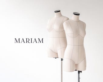 May include: Two beige dress forms with black accents stand against a white backdrop. The forms have a classic design with marked seam lines. The word "MARIAM" is displayed in elegant, dark lettering on the left.