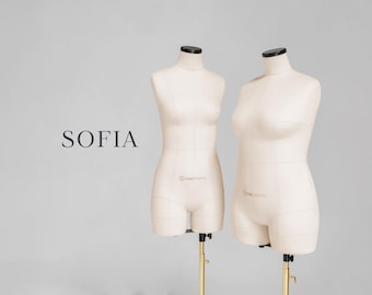 Pode incluir: Dois manequins bege com tampas pretas e suportes dourados são exibidos em um fundo cinza claro. A palavra "SOFIA" está impressa em preto no lado esquerdo. Os manequins são projetados para simular a forma de um torso humano.