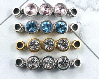 May include: Four rows of gemstone connectors in various colors. The top row has pink gemstones, the second row has blue gemstones, the third row has clear gemstones with gold settings, and the bottom row has clear gemstones with silver settings.