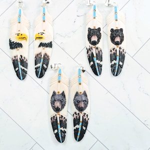May include: Hand-carved feather pendants with silver-tone findings. The pendants feature detailed carvings of an eagle, bear, and wolf. Each feather is cream-colored with black, blue, and turquoise accents. These pendants are ideal for Native American-inspired jewelry.