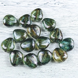 May include: A collection of 15 green and gold iridescent glass beads in a teardrop shape. The beads are scattered on a white wooden surface.