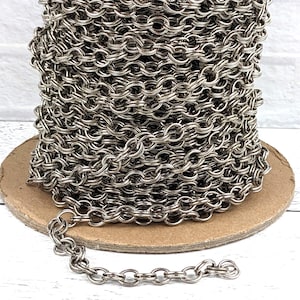 May include: A spool of silver chain, wound tightly and ready to be used for jewelry making or other crafting projects.