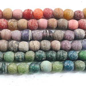 May include: Rows of colorful, textured beads in various shades of red, orange, pink, brown, purple, green, and blue. The beads appear to be made of stone or a similar material, with a slightly rough surface.