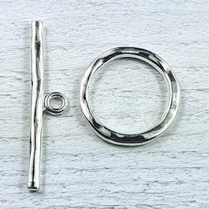 May include: Silver toggle clasp with a hammered finish. The clasp is made of two pieces: a bar and a ring.