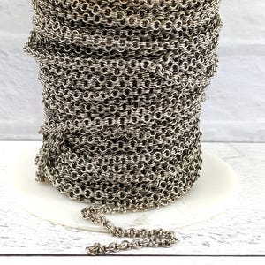 Puede incluir: Un rollo de cadena plateada, enrollado y listo para ser utilizado en la elaboración de joyas. La cadena está hecha de pequeños círculos unidos.