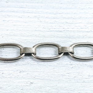 Może przedstawiać: Zbliżenie srebrnego łańcucha z owalnymi ogniwami. Łańcuch jest wykonany z metalu i ma polerowane wykończenie.