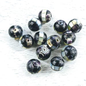 May include: A group of black and white round beads with a mosaic pattern. The beads are made of a material that resembles mother of pearl.