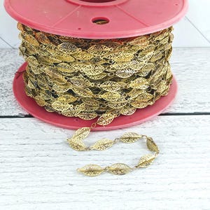 May include: A spool of gold leaf chain trim with a pink plastic spool. The chain is made of small, delicate, openwork leaves.