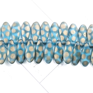 May include: A collection of blue teardrop-shaped beads with gold polka dots. The beads are arranged in two rows, creating a visually appealing pattern. The beads are likely for jewelry making.