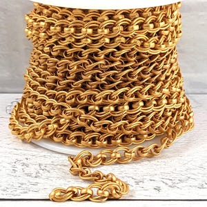 May include: A spool of gold-coloured chain trim. The chain is made of metal and has a woven design. The chain is coiled on a white spool.