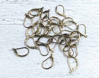 May include: A pile of gold-toned earring hooks, also known as ear wires, for jewelry making. The hooks are made of metal and have a teardrop shape.