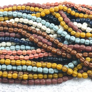 May include: A selection of multi-coloured, vintage-style beads in shades of brown, yellow, blue, pink, and white. The beads have a ribbed texture and are strung together, creating a visually appealing display.