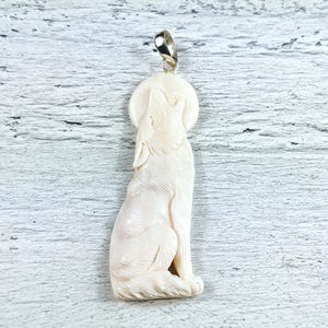 May include: A white bone pendant carved in the shape of a wolf howling at the moon. The pendant is attached to a silver bail.