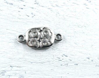 May include: Silver-toned metal connector with a floral design. The connector has two loops on either side for attaching jewelry.
