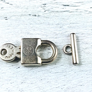 May include: Silver-toned metal clasp with a padlock design and a separate toggle bar. The padlock has a keyhole and the text "Made in Italy" engraved on the side.
