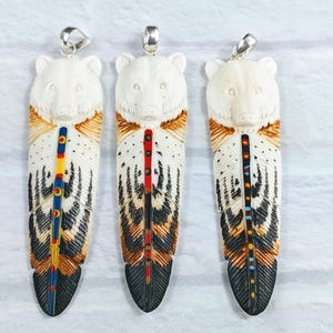 May include: Three bear-shaped pendants with feather designs. The bear heads are white, transitioning to brown and black feather patterns. Each pendant has a silver-colored bail for hanging. The feathers have colorful accents of red, yellow, and blue.