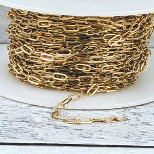 May include: A spool of gold-colored chain with a small section of chain extending from the spool. The chain is made of small, oval-shaped links.