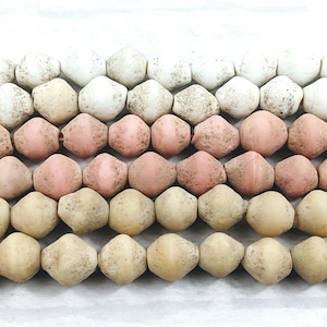 May include: A strand of beads in three colours: white, light pink, and beige. The beads are faceted and have a rough, textured surface.