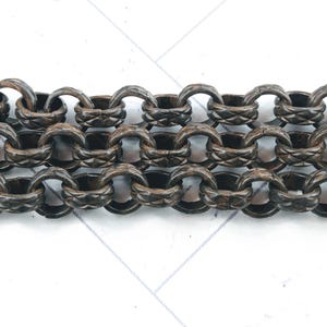May include: A close-up of a dark brown wooden chain with intricate carvings. The chain is made of multiple linked rings, each with a diamond-shaped pattern.