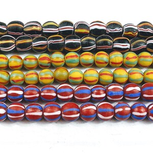 May include: A collection of colorful glass beads with striped patterns. The beads are arranged in rows, with the top row featuring black and white stripes, the second row featuring yellow and red stripes, and the bottom row featuring red and blue stripes.