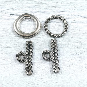 May include: Four silver metal toggle clasps. Two are round and two are rectangular with a rope design.