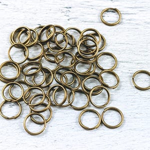 以下が含まれることがあります： ジュエリー作りに使用される金属製のリングの一種である、金色のジャンプリングの山。