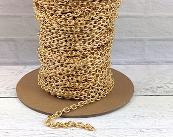 May include: A spool of gold-colored chain, tightly wound and ready for use. The chain is made of small, oval links, and a portion of the chain extends from the spool. The chain sits on a brown cardboard base.