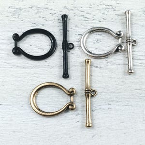 May include: Four different styles of metal toggle clasps. Two are silver, one is gold, and one is black.