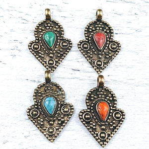 Könnte beinhalten: Vier verzierte goldene Anhänger mit verschiedenen Edelsteineinsätzen. Jeder Anhänger hat ein detailliertes Design mit einem tropfenförmigen Edelstein in der Mitte. Die Edelsteine sind türkis, rot, blau und orange.