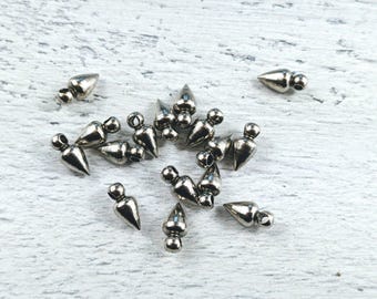 May include: A group of silver metal pyramid-shaped charms with a loop at the top. The charms are scattered on a white wooden surface.
