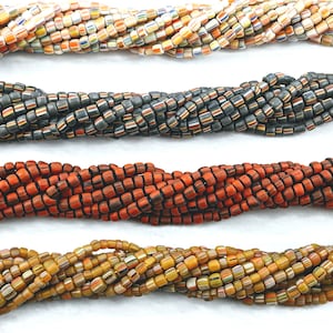 May include: Four strands of colourful glass beads, each strand featuring a different colour combination. The top strand is white with orange, yellow, and blue stripes. The second strand is black with orange, yellow, and blue stripes. The third strand is orange with black stripes. The bottom strand is yellow with orange, white, and black stripes.