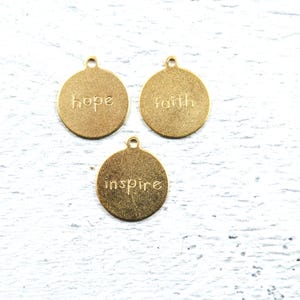 May include: Three gold-colored metal charms with the words "hope", "faith", and "inspire" engraved on them.