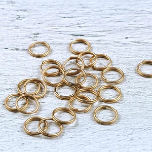 May include: A pile of gold jump rings, a type of jewelry finding, on a white wooden surface.