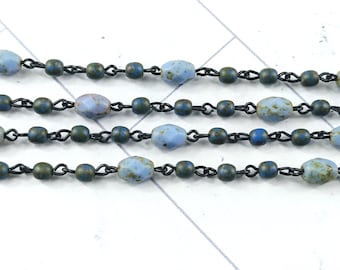 May include: Close-up of several strands of beaded jewelry. The beads are a mix of light blue and dark green, with a matte finish. The beads are connected by small, dark metal links.