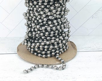 May include: A spool of silver metal chain with round links. The chain is coiled on a brown cardboard spool.